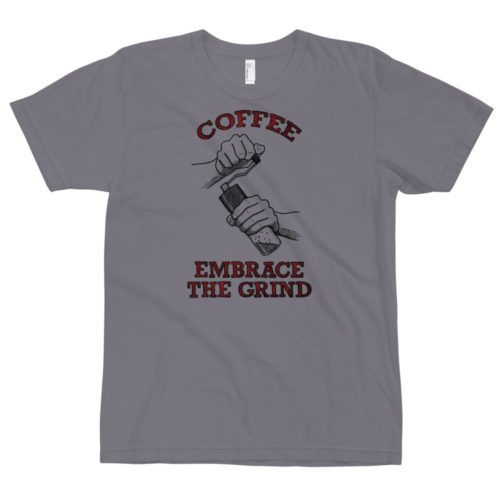 A slate gray t-shirt with a drawing of hands using a handheld coffee grinder with the words COFFEE EMBRACE THE GRIND in yellow lettering. Designed by Kenny Velez