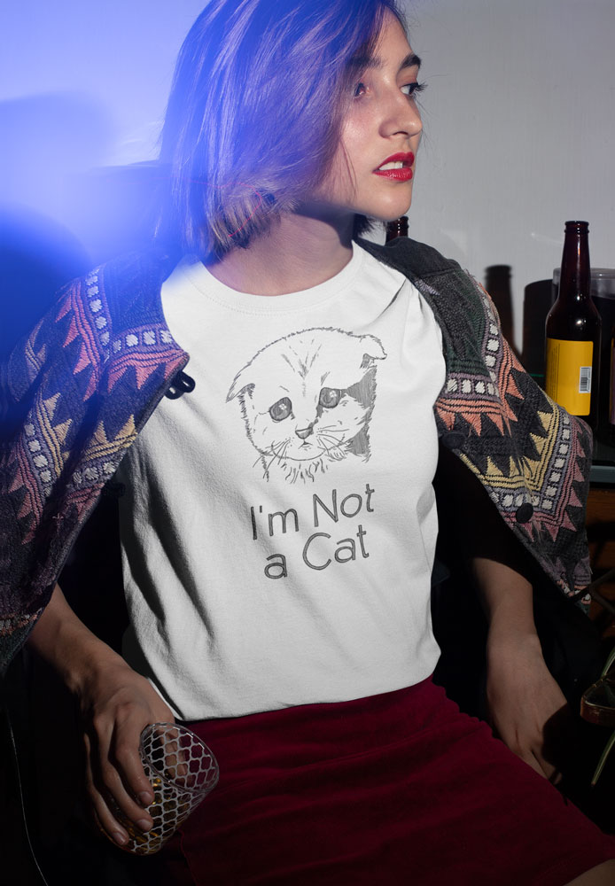 A girl at a house party wearing a white t-shirt with a drawing of a sad cat with the words I'm Not a Cat. Designed by Kenny Velez.