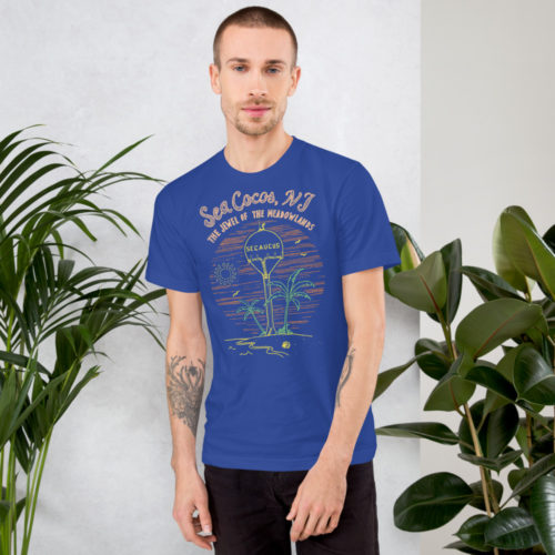 A man wearing a royal blue t-shirt with a drawing of the water tower from Secaucus, NJ on a beach with the words Sea Cocos, The Jewel of the Meadowlands. Designed by Kenny Velez.