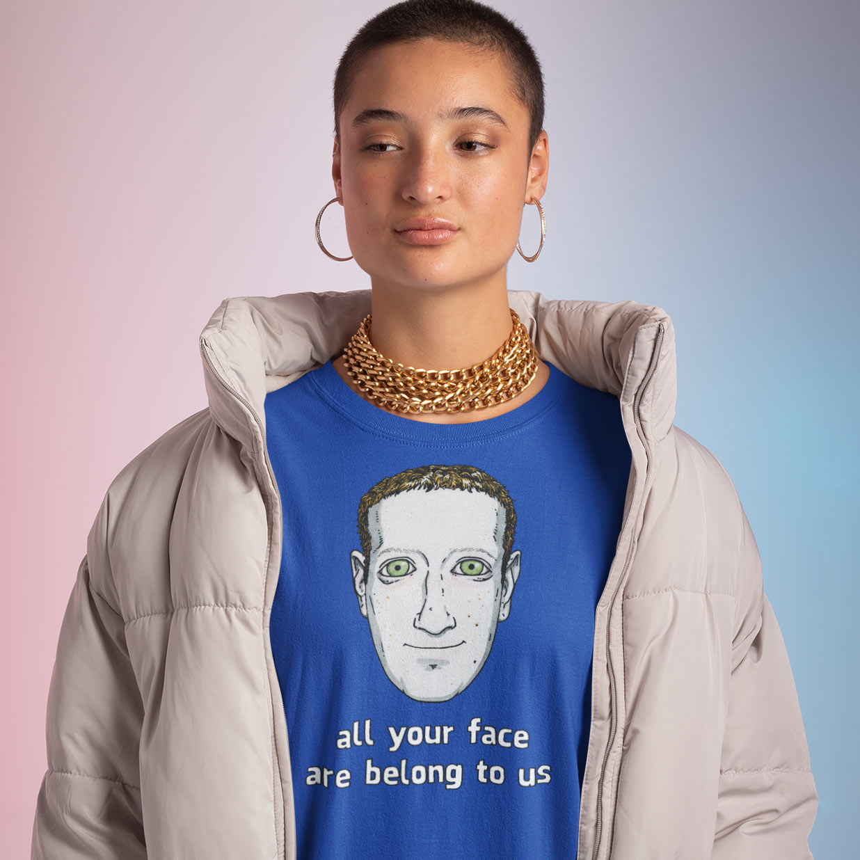 A woman wearing an oversized puffy and a royal blue t-shirt with a creepy drawing of Mark Zuckerberg with the words All Your Face Are Belong To Us. Designed by Kenny Velez