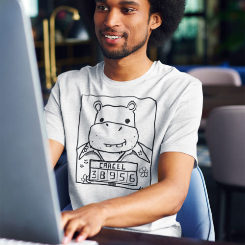 A guy on a computer wearing a t-shirt with a drawing of a mugshot featuring a cartoon hippo in a Hawaiian shirt in the vein of the iconic mugshot of Pablo Escobar. Designed by Kenny Velez.