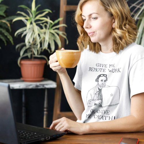 A woman on a laptop wearing a white t-shirt with a drawing of founding father Patrick Henry working on a laptop with the words GIVE ME REMOTE WORK OR GIVE ME DEATH! Designed by Kenny Velez