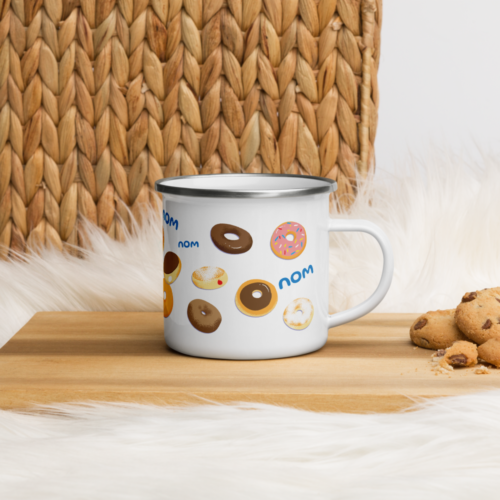 a white camper mug with a cute cartoon squirrel eating a doughnut and surrounded by donuts with the words nom