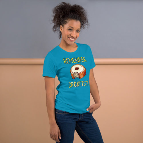 A woman wearing a blue t-shirt with a drawing of a bitten cronut with the words REMEMBER CRONUTS? in yellow lettering. Designed by Kenny Velez.