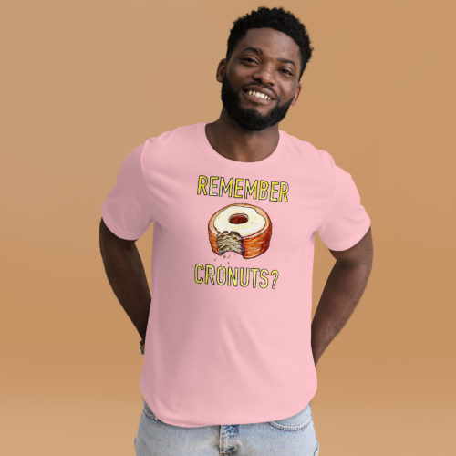 A man wearing a pink t-shirt with a drawing of a bitten cronut with the words REMEMBER CRONUTS? in yellow lettering. Designed by Kenny Velez.