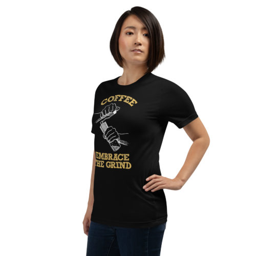 a girl wearing A black t-shirt with a drawing of hands using a handheld coffee grinder with the words COFFEE EMBRACE THE GRIND in yellow lettering. Designed by Kenny Velez