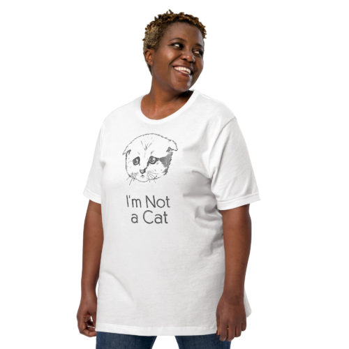 A woman wearing a white t-shirt with a drawing of a sad cat with the words I'm Not a Cat. Designed by Kenny Velez.