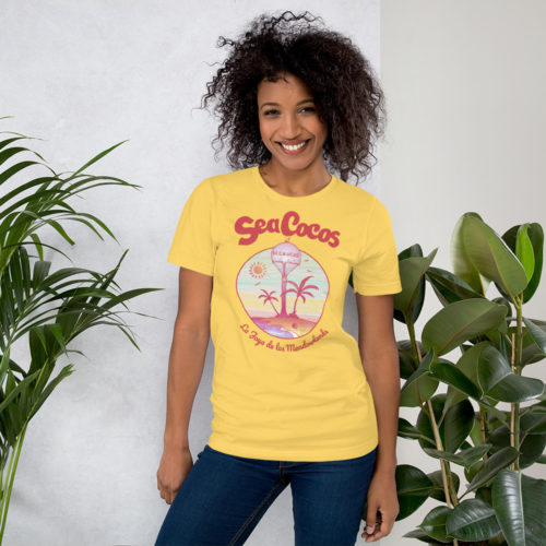 a girl wearing a yellow color t-shirt with a drawing of the water tower from Secaucus, NJ on a beach, with the words Sea Cocos, La Joya de los Meadowlands. Designed by Kenny Velez.