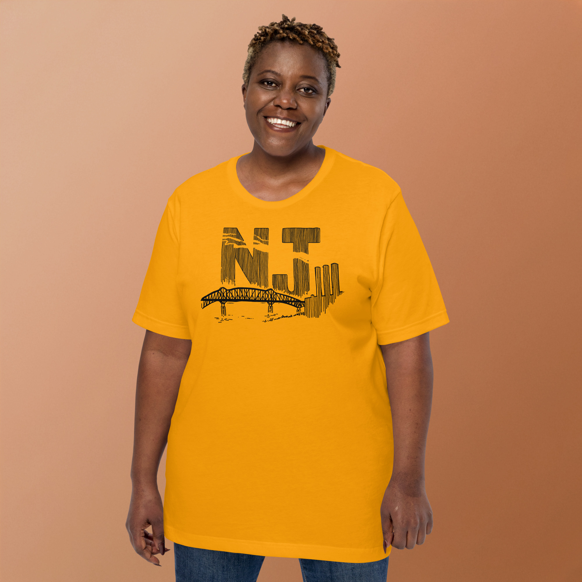 A woman wearing a gold colored t-shirt with a line drawing of the Pulaski Skyway and Kearny power plant with the initials NJ. Designed by Kenny Velez.