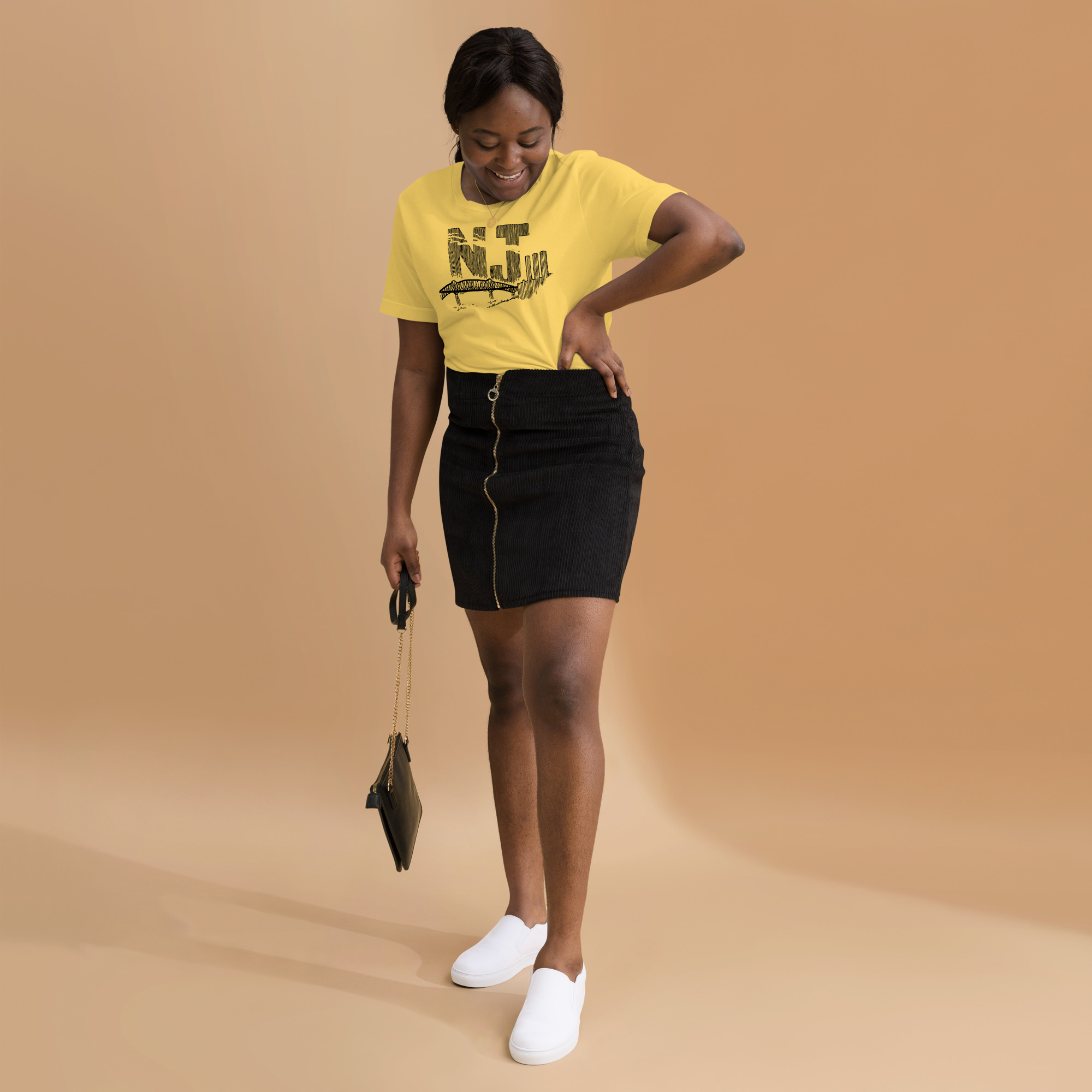 A woman wearing a yellow t-shirt with a line drawing of the Pulaski Skyway and Kearny power plant with the initials NJ. Designed by Kenny Velez.